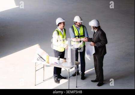 Ein leitender Geschäftsmann mit Architekt, der mit einem jungen Ingenieur die Hand schüttelt, auf der Baustelle auf leeren Flächen, Immobilieninvestoren konstruieren Stockfoto