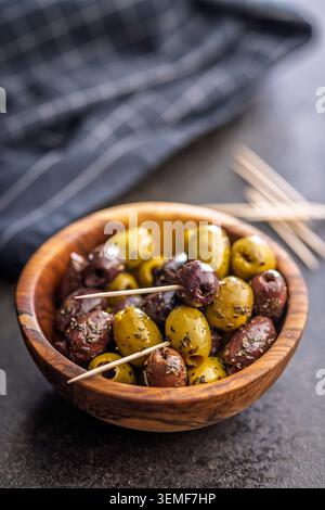 Marinierte grüne und Kalamata-Oliven serviert in einer rustikalen Holzschale mit Zahnstochern und einer Flasche Olivenöl, perfekt für mediterrane Vorspeisen, sn Stockfoto