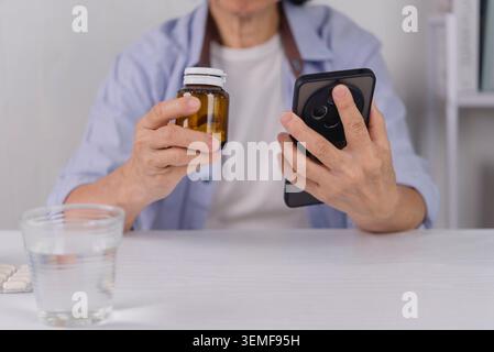 Nahaufnahme der Hände einer Seniorin, die eine Arzneiflasche hält und die Smartphone-App verwendet. Gesundheitstechnologie für ältere Menschen, telemedizinische Beratung und Online Stockfoto