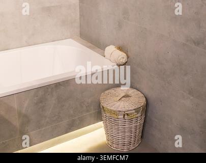 Badeecke aus weißem Acryl mit gerolltem Handtuch und gewebtem Korb auf dem Boden Stockfoto