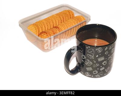 Eine Tasse heißer brauner Milchkaffee in einer schwarzen Tasse mit weißen Retro-Abbildungen, neben einem durchsichtigen Kunststoffbehälter mit runden Keksen auf einem hellweißen Hintergrund Stockfoto