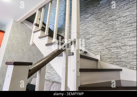 Eine Treppe mit weißen Geländern und dunklen Stufen führt gegen eine Kunststeinmauer. Stockfoto