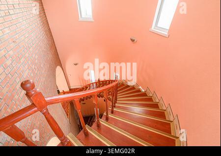 Hochwinkelaufnahme einer Wendeltreppe in einem Gebäude mit pfirsichfarbenen Wänden. Die Treppen sind aus Holz mit dekorativen Akzenten. Stockfoto