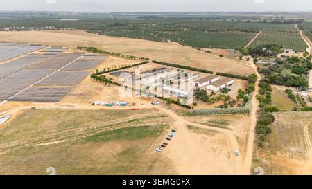 Erhöhter Blick auf ein großes Solarkraftwerk neben landwirtschaftlichen Feldern und Bauernhäusern in Coria del Rio, Spanien Stockfoto