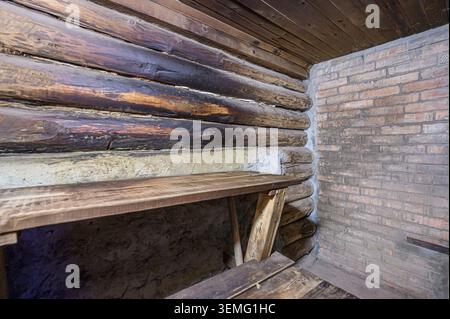 Rustikale Ecke mit einer Holzwand und einer Holzbank im Kontrast zu einer Backsteinmauer. Die Decke besteht aus Holz. Stockfoto
