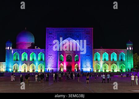 Abendlicher Blick auf Tilya Kori Madrasah in Samarkand mit farbenfroher Nachtbeleuchtung, während Touristen in der Nähe der beleuchteten Fassade spazieren., 14. September 2024 Sam Stockfoto