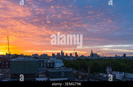 Panorama-Skyline von London bei Sonnenaufgang mit leuchtenden orangefarbenen Wolken über der Stadt und grünem Park im Vordergrund, England, Großbritannien Stockfoto