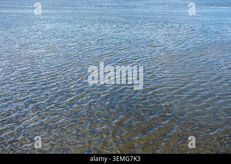 Blaues Wasser plätschert sanft an einer breiten Flussoberfläche. Stockfoto