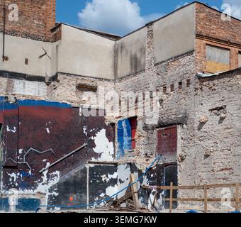 Das teilweise abgerissene Backsteingebäude zeigt freiliegende strukturelle Elemente und alte Graffiti. Stockfoto