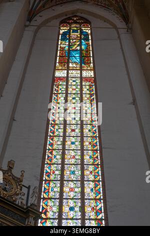 Das hohe Buntglasfenster beleuchtet eine weiße Putzwand in einem historischen religiösen Gebäude. Stockfoto