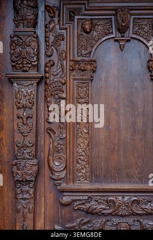 Der kunstvoll geschnitzte hölzerne Türbereich zeigt detaillierte Gesichter und Blumenmuster an einem historischen Eingang. Stockfoto