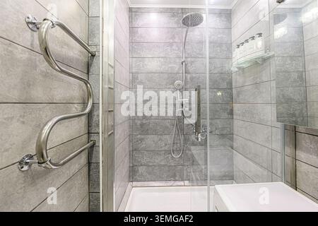 Modernes Bad mit einer verglasten Dusche mit grauen Fliesenwänden und einem eleganten Handtuchwärmer aus Chrom Stockfoto