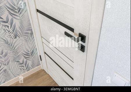 Nahaufnahme einer weißen Tür mit schwarzen Beschlägen und gemusterten Tapeten Stockfoto