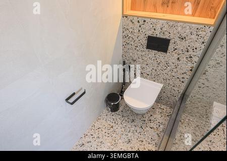 Die Hochwinkelaufnahme zeigt eine moderne Badezimmerecke mit weiß gefliesten Wänden, Terrazzo-Boden und eleganter Toilette Stockfoto
