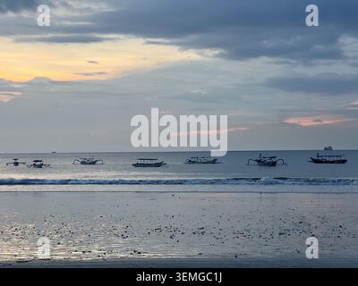 Traditionelle Fischerboote von Jukung, die bei Sonnenuntergang an einem ruhigen Strand vor der Küste ankern, Bali, Indonesien. Stockfoto