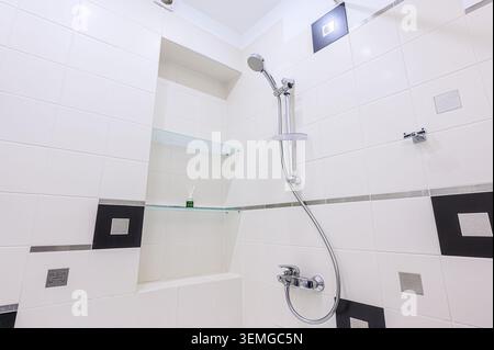 Modernes Bad mit Dusche. Weiße und schwarze Fliesen, Glasböden und eine Chrom-Duschvorrichtung. Klares und einfaches Design Stockfoto