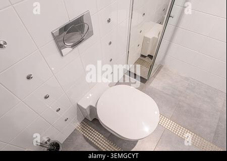 Das saubere Bad ist mit weißen Fliesenwänden, grauem Fliesenboden, weißer Toilette und Chromarmaturen ausgestattet. Stockfoto