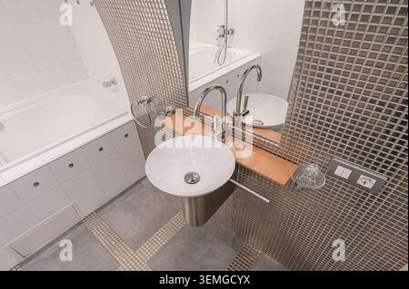 Modernes Bad mit rundem, weißem Waschbecken, Mosaikfliesen, Badewanne und klaren Linien. Das Design betont Funktionalität und minimalistische Ästhetik Stockfoto