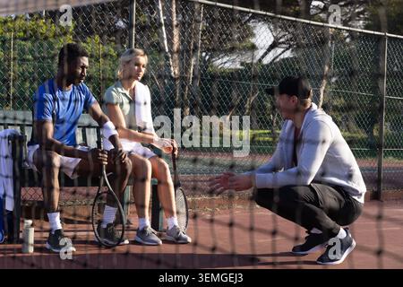 Diverse Tennisspieler und Trainer sitzen und diskutieren Strategie auf dem Parkplatz mit Handtuch, Schlägern Stockfoto