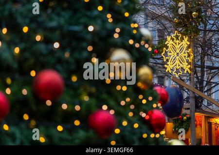 Decorated Christmas tree with golden lights and ornaments, a glowing snowflake, and market stall Stockfoto
