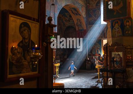 Ein kleiner Junge spaziert durch die Upper Betlemi Kirche, umgeben von religiösen Ikonen und goldenen Lichtstrahlen in Tiflis, Georgia. Stockfoto
