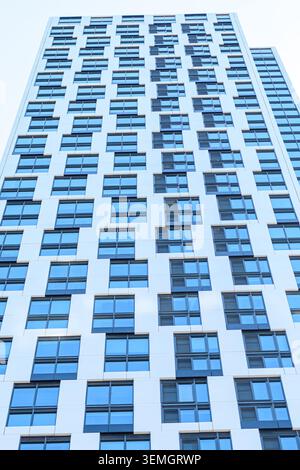 Moderne Hochhausfassade mit einem Gitter aus blau getönten Fenstern und weißen Verkleidungstafeln von unten. Stockfoto