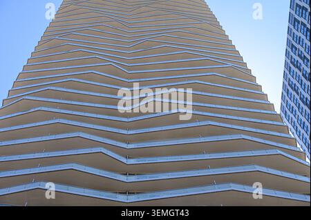Flacher Blick auf einen Wohnturm mit gestapelten Zickzack-Balkonen und Glasgeländern. Stockfoto
