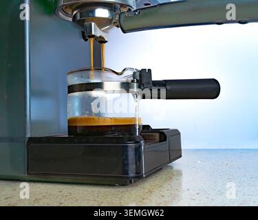 Espressomaschine, die Kaffee in einer Glasbecher zubrüht, die Zubereitung von Getränken in der Hausküche für die morgendliche Routine, Koffein, Lifestyle und Getränkekonzept, das heute verwendet wird. Stockfoto