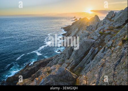 Goldener Sonnenuntergang über der dramatischen felsigen Küste mit Leuchtturm Silhouette in Pointe du Raz, Bretagne, Frankreich Stockfoto