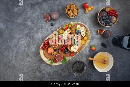 Frühstück mit Pfannkuchen, Beeren, Feigen und Honig auf dunkler strukturierter Oberfläche Stockfoto