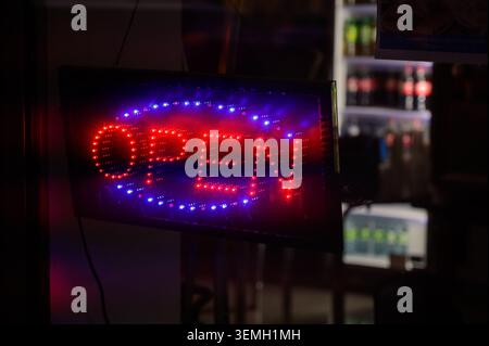 Das rote und blaue LED-Schild „OPEN“ leuchtet hell in einem schwachen Schaufenster Stockfoto