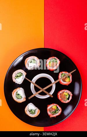 Kreative flache Lage mit verschiedenen Sushi-Rollen auf Kreisplatte auf rotem Hintergrund Stockfoto