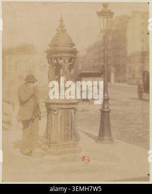 Ein Wallace-Brunnen steht 1898 in Paris, fotografiert von Eugène Atget. Die Struktur ist Teil der städtischen Umgebung und erscheint innerhalb einer Pariser Manierszene, die zwischen 1870 und 1913 dokumentiert wurde. Stockfoto