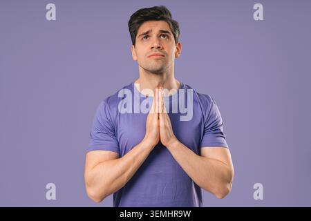 Reifer Mann betet mit Palmen auf violettem Hintergrund. Guy fleht Wünsche befriedigen Stockfoto