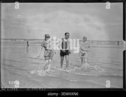 Badegäste spazieren 1923 am Strand von Deauville entlang. Das Pressefoto zeigt Menschen, die sich an der Küste entlang der Kanalküste bewegen und die Freizeitaktivitäten im Normandie-Resort reflektieren. Stockfoto