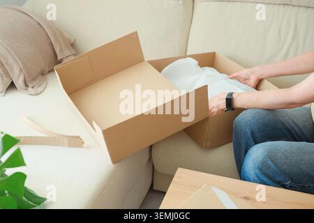 Mittlere ältere Frau packt Karton nach Online-Einkäufen zu Hause aus Stockfoto