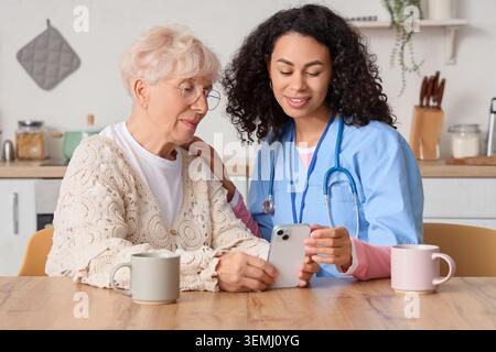 Afroamerikanische Krankenschwester mit Seniorin am Tisch in der Küche Stockfoto