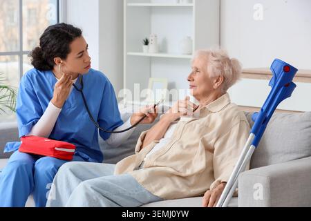 Afroamerikanische Pflegekraft mit Stethoskop, die kranken Seniorinnen im Pflegeheim zuhört Stockfoto