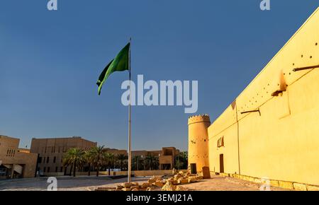 Die historische Festung Masmak aus Lehm und Lehmziegel unter einem blauen Himmel mit der saudischen Nationalflagge, die in Riad, Saudi-Arabien, weht. Stockfoto