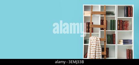 Weißes Bücherregal mit Büchern und Holzleiter vor blauer Wand mit Kopierraum, gemütlichem Innenraum der Bibliothek, Lese- und Bildungskonzept Stockfoto
