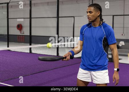 Afroamerikaner in blauem Hemd mit schwarzem Paddel, gelber Ball auf lila Court, Kopierraum Stockfoto