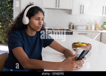 Afrikanische Frau, die auf der Kücheninsel sitzt, trägt ein marineblaues Hemd und ein Headset mit Telefon, Kopierraum Stockfoto