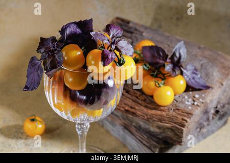 Gelbe Kirschtomaten mit violettem Basilikum in rustikalem Kristallglas Stockfoto