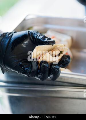 Nahaufnahme eines Kochs mit Handschuhen, der während der Zubereitung in einer Küche oder einem Catering in Frankreich Lebensmittel hält. Stockfoto