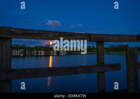 Der hölzerne Zaun eines Piers rahmt im Vordergrund den eindrucksvollen Blick auf den See Les Pouyades bei Nacht. Der Vollmond scheint während der durch die Wolken Stockfoto