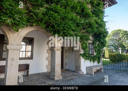 Eine bezaubernde Steinhausfassade in Ribadeo, bedeckt mit üppigem grünem Klettereifeu, mit einer traditionellen bogenförmigen Veranda und Holzbänken. Stockfoto