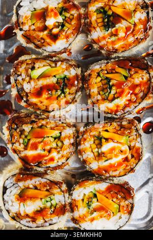 Sushi-Brötchen werden ordentlich auf einen Teller mit bunten Füllungen gelegt. Saucen werden über die Brötchen getränkt. Diese Szene zeigt Speisen, die zum Genießen bereit sind Stockfoto