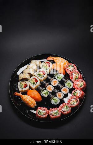 Eine runde schwarze Platte bietet Platz für Sushi und Brötchen mit verschiedenen Arten von Fisch, Reis und Gemüse. Die Platte ist für Servierzwecke und Präsentationen angeordnet Stockfoto