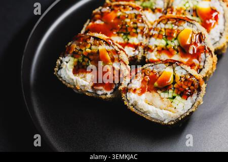 Sushi-Rollen werden auf eine schwarze Platte gelegt. Die Brötchen werden mit Soße belegt und umfassen Fisch und Gemüse. Sie sind ordentlich angeordnet und bereit, du zu essen Stockfoto