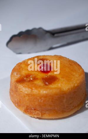 Bäckerei und Konditorei, kulinarische Kunst und Tradition Mexikos. Ananas auf dem Kopf mit einer Kirsche oben, mit einer Küchenzange im Hintergrund, vertikal Stockfoto